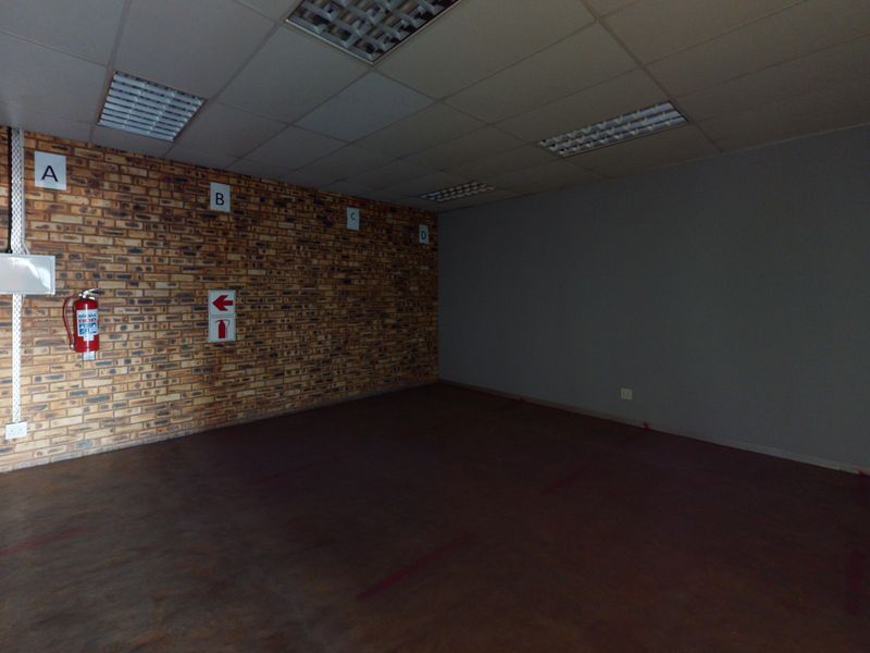 An empty commercial office space featuring an exposed brick feature wall, suspended ceiling with recessed lighting, and essential fire safety equipment.