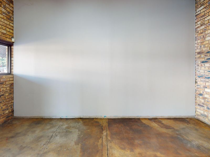 An empty commercial space featuring exposed brick side walls, a central painted wall, and stained concrete flooring with an exterior window.