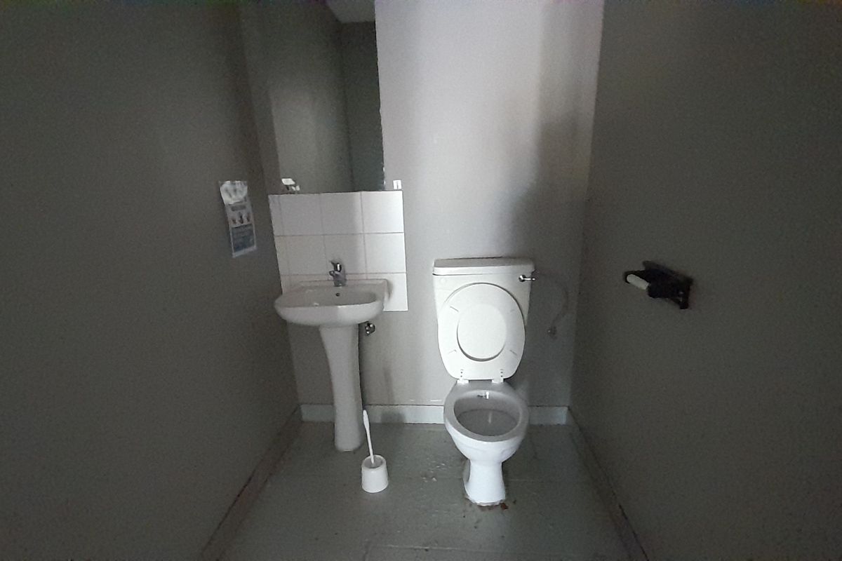 A small, functional office restroom featuring a pedestal washbasin and a standard toilet with a tiled splashback.