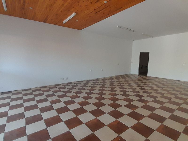 A spacious, empty office area featuring a timber-paneled ceiling, fluorescent lighting, and distinctive checkered ceramic floor tiles.