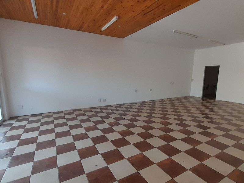 An empty, open-plan office space featuring a timber ceiling, checkered tile flooring, and a glass sliding door providing natural light.