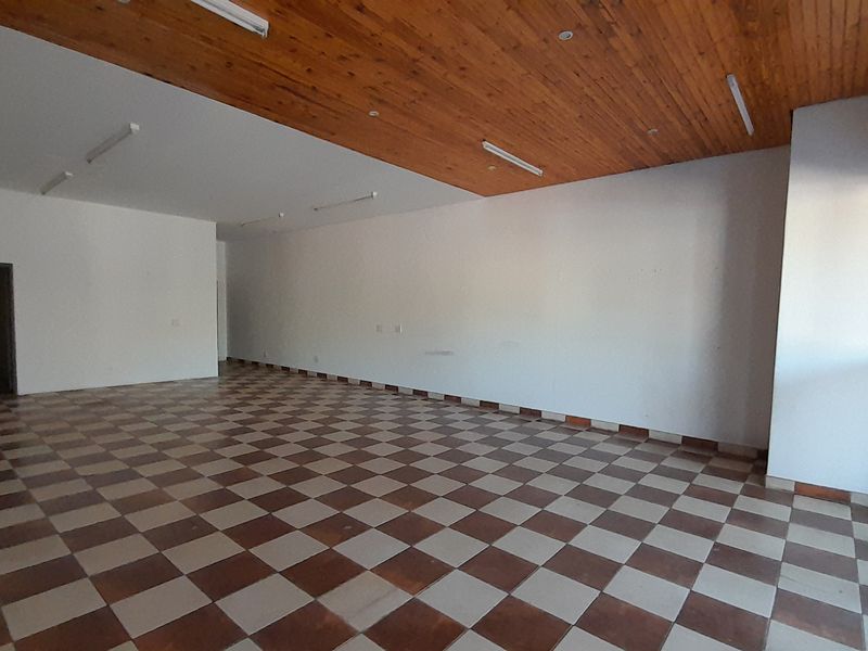 Spacious open-plan office area featuring a wooden ceiling, checkered tile flooring, and large glass sliding doors providing natural light.