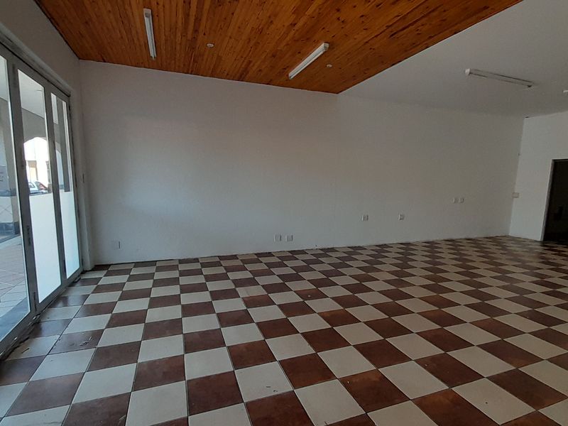 Spacious, empty office unit featuring a timber ceiling, checkered ceramic floor tiles, and large aluminium sliding glass doors providing natural light.
