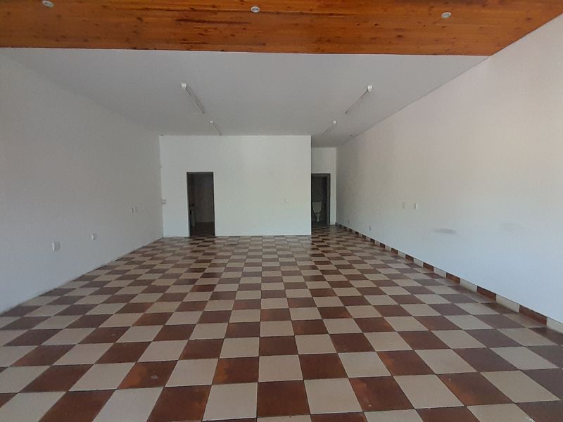 A spacious, empty office area featuring a timber ceiling, checkered ceramic floor tiles, and neutral white walls, suitable for various commercial configurations.