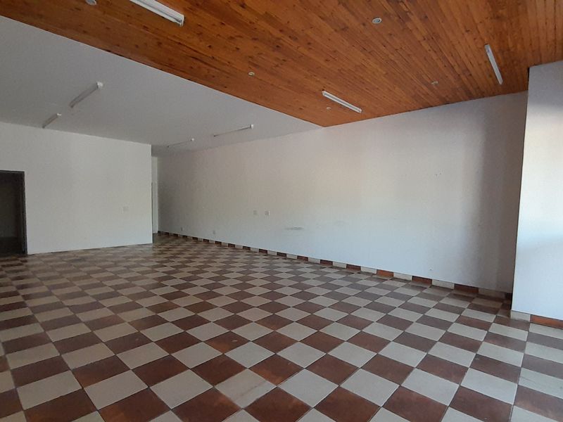 Spacious, empty office area featuring a timber ceiling, checkered tiled flooring, and large sliding glass doors providing natural light.