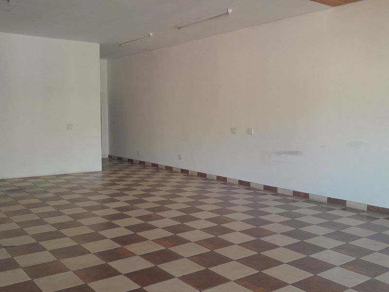 A vacant, open-plan office space featuring checkered ceramic floor tiles, neutral walls, and overhead fluorescent lighting, ready for custom fit-out.