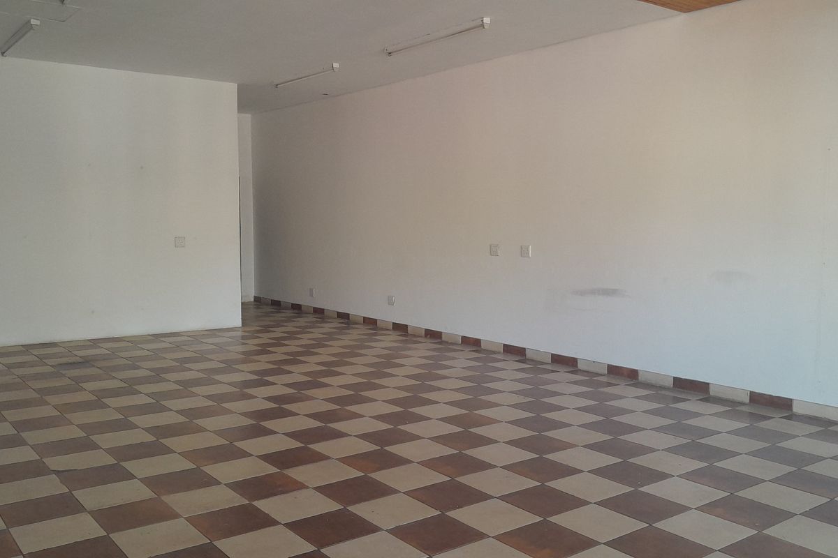 A vacant, open-plan office space featuring checkered ceramic floor tiles, neutral walls, and overhead fluorescent lighting, ready for custom fit-out.