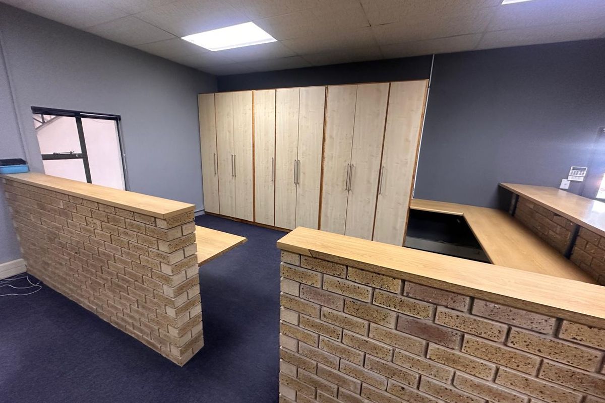 Spacious office area featuring built-in storage cabinetry, brick partition walls with integrated desk surfaces, and a suspended ceiling with recessed lighting.
