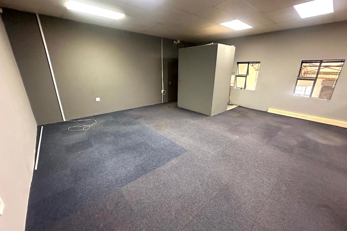 An open-plan industrial office space featuring carpet tiles, suspended ceilings with recessed lighting, and a central partition wall.