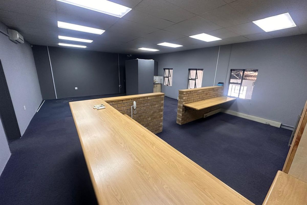 Spacious open-plan office area featuring built-in brick counters, carpeted flooring, suspended ceilings with recessed lighting, and integrated air conditioning.