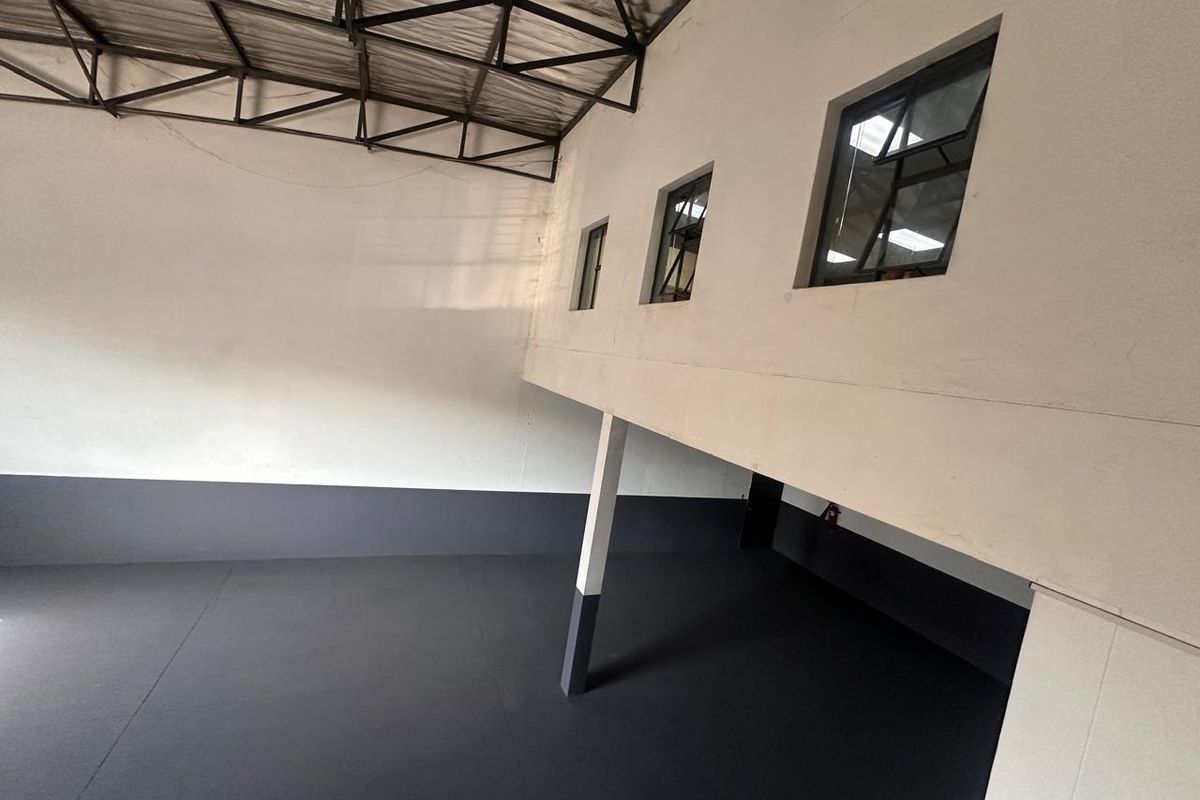Spacious industrial utility area featuring high exposed steel roof trusses, painted concrete flooring, and natural light through multiple steel-framed windows.