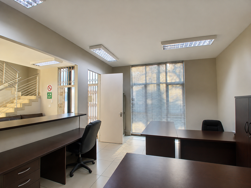 A professional office space featuring tiled flooring, built-in reception desk, fluorescent lighting, and secure access points with security gates.