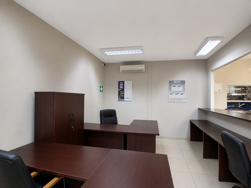 A functional office space featuring tiled flooring, integrated fluorescent lighting, a wall-mounted air conditioning unit, and a built-in service counter.