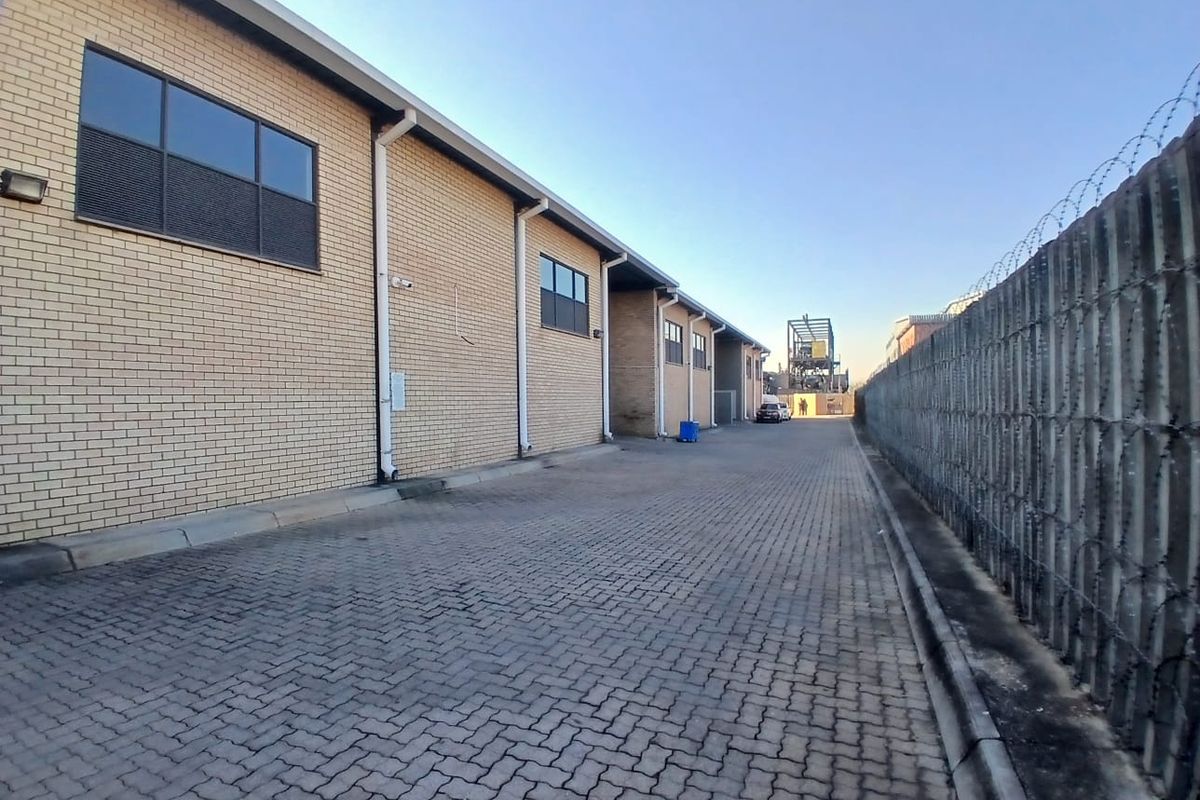 Side access driveway of an industrial property featuring brick facade, paved surface, and secure perimeter fencing with razor wire.