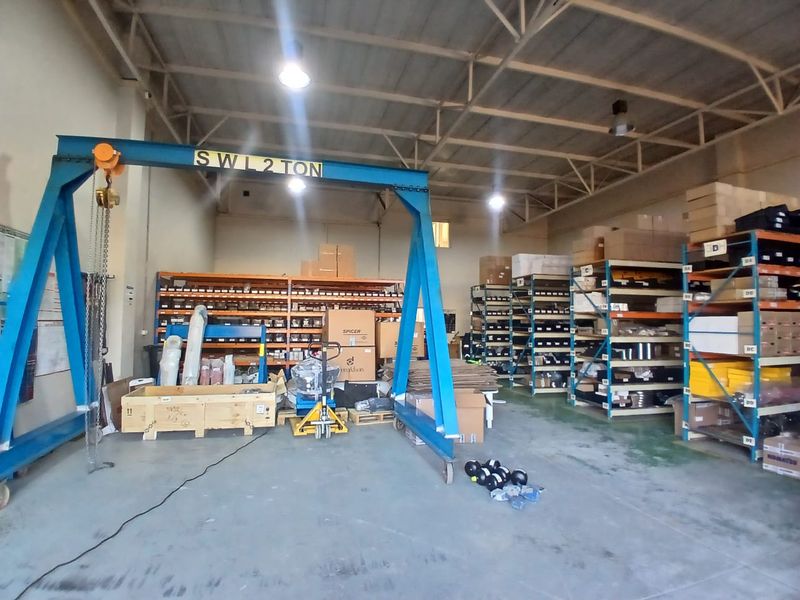 Industrial warehouse space featuring a 2-ton gantry crane, extensive metal shelving units, exposed steel roof structure, and durable concrete flooring.
