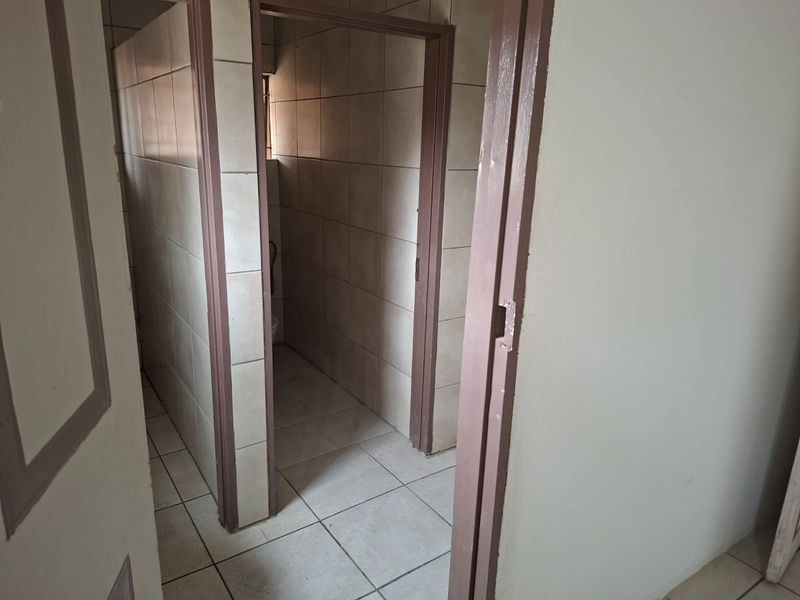 A functional commercial bathroom space featuring tiled walls and flooring with multiple partitioned cubicles.