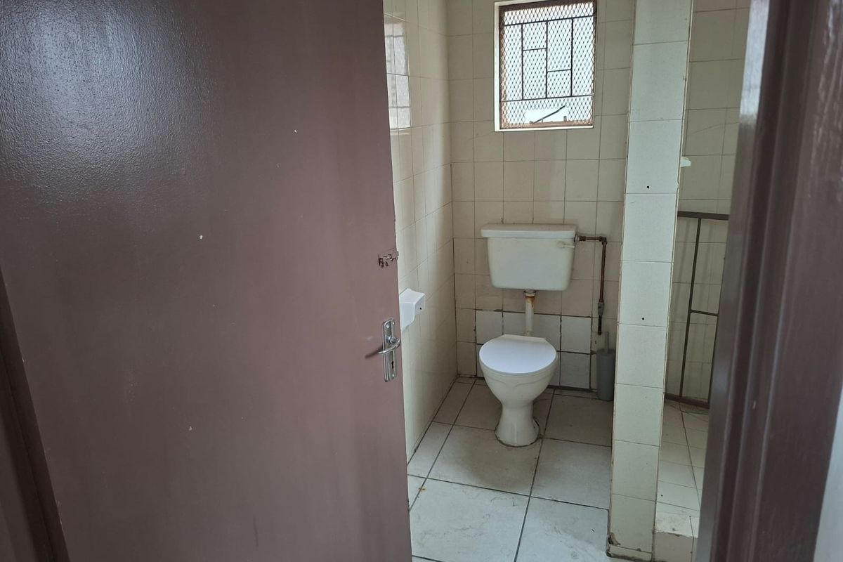 A functional, compact bathroom featuring tiled walls and flooring, a standard toilet, and a window with a security grille.