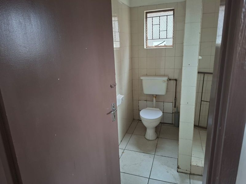 A functional, compact bathroom featuring tiled walls and flooring, a standard toilet, and a window with a security grille.