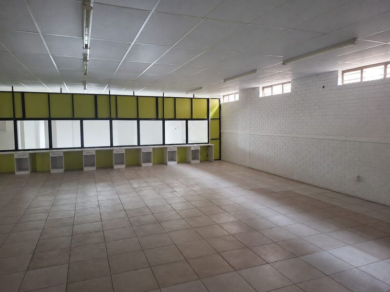 A spacious, empty commercial office area featuring tiled flooring, built-in desk partitions, and functional overhead lighting, suitable for a variety of business configurations.