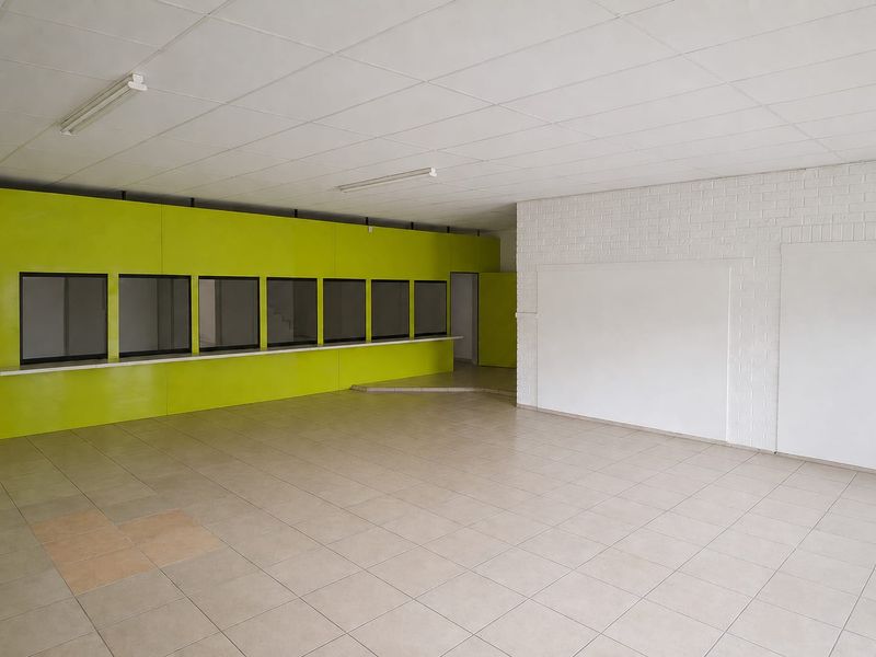An empty commercial office space featuring a long service counter, tiled flooring, and a suspended ceiling, suitable for various business or retail applications.