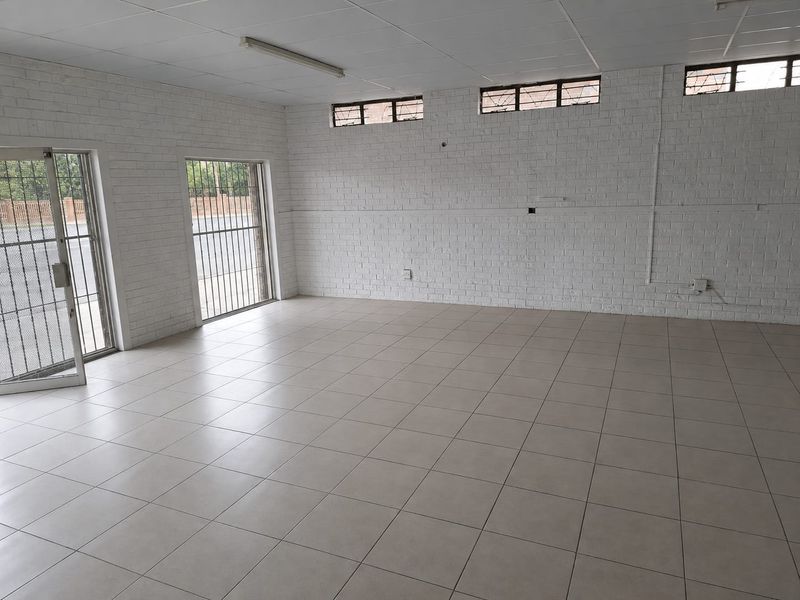 A vacant commercial office space featuring tiled flooring, painted brick walls, and security bars on windows, providing a clean and functional layout.