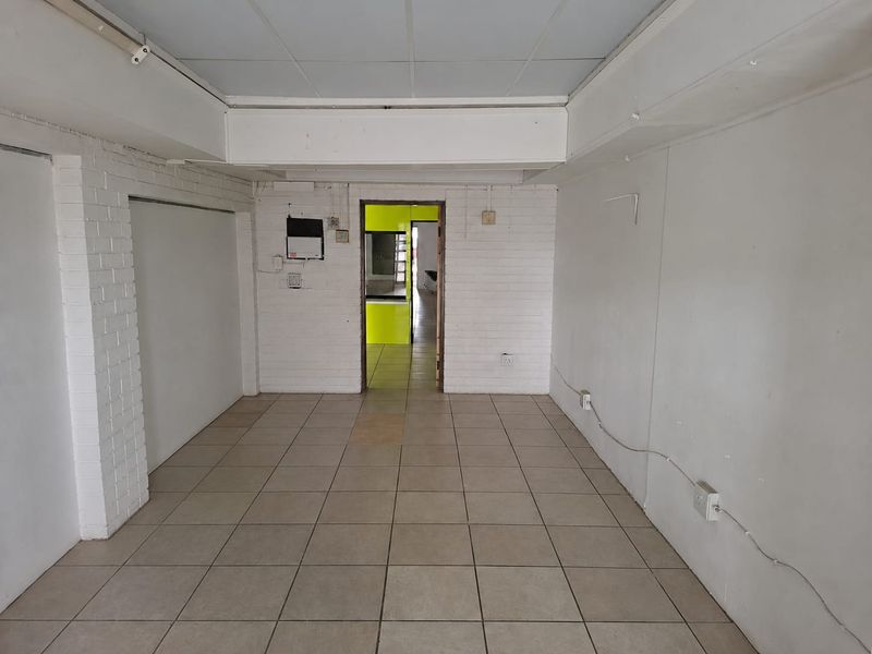 An empty commercial office space featuring tiled flooring, exposed brick walls, and a drop ceiling, providing a blank canvas for business customization.