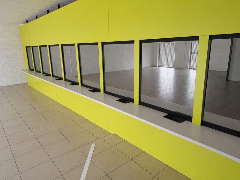 Commercial service area featuring a long counter with multiple security glass partitions, tiled flooring, and secure window bars.
