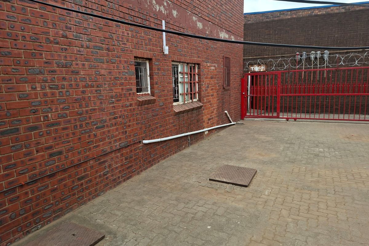 Rear exterior view of a commercial property featuring a brick facade, paved yard, and secure gated access with razor wire fencing.