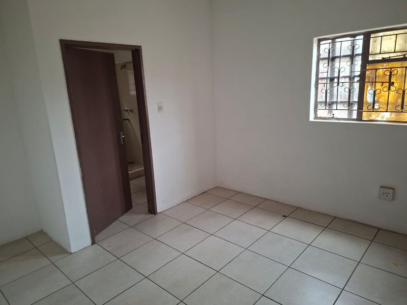 An empty bedroom featuring tiled flooring, a window with security bars, and direct access to an adjoining bathroom.
