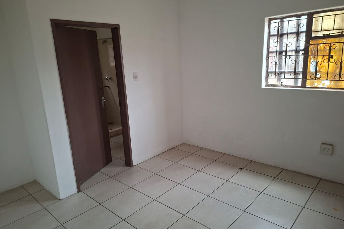 An empty bedroom featuring tiled flooring, a window with security bars, and direct access to an adjoining bathroom.
