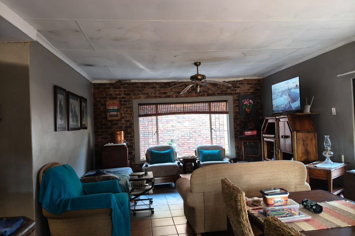 Living room featuring an exposed brick feature wall, tiled flooring, and a ceiling fan, with visible water damage on the ceiling.