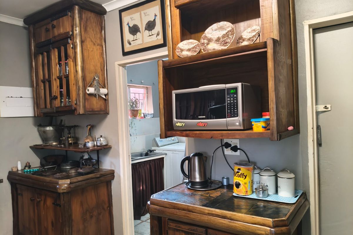 A rustic kitchen featuring custom timber cabinetry and tiled countertops, with a view through to an adjacent scullery or laundry area.