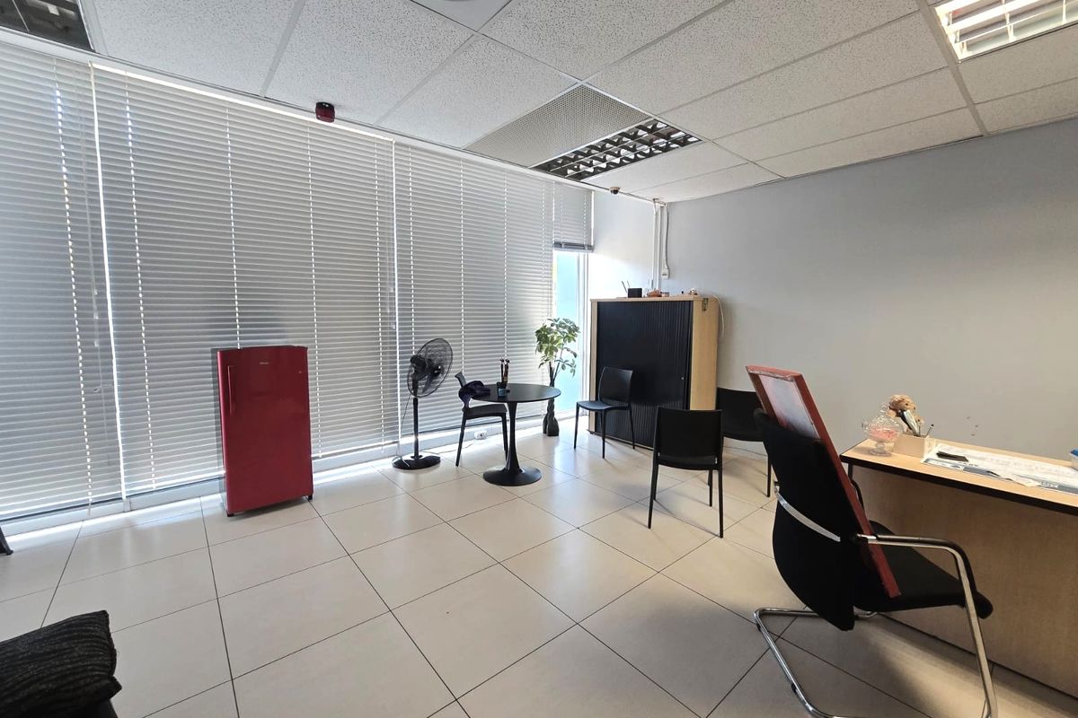 A functional office space featuring tiled flooring, a suspended ceiling with recessed lighting, and large windows fitted with venetian blinds.