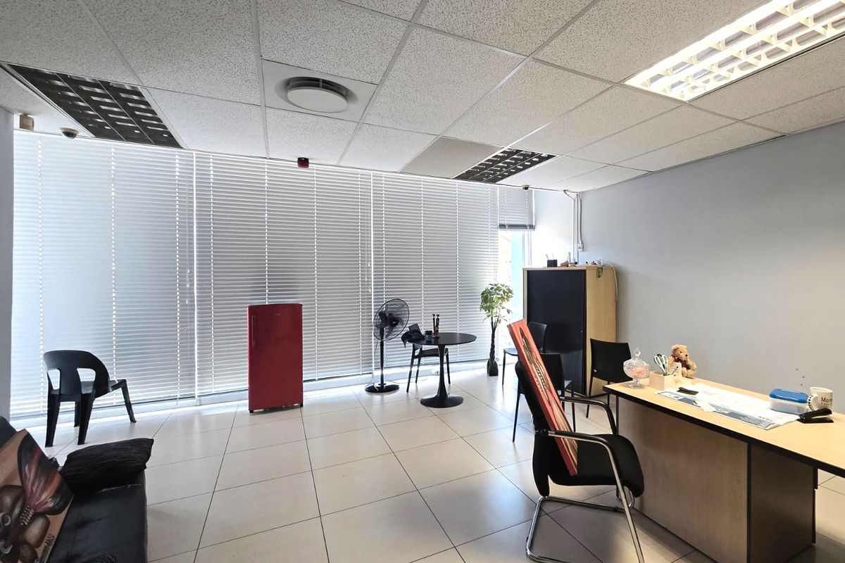 A functional office space featuring tiled flooring, a suspended ceiling with integrated lighting, and large windows fitted with venetian blinds.