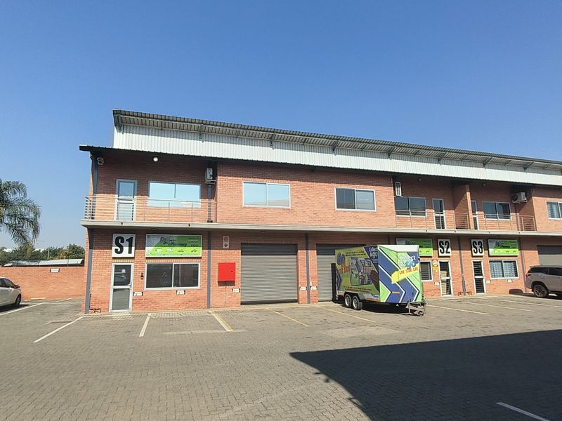 Front elevation of a multi-unit industrial complex featuring brick construction, metal roller shutter doors, and paved parking facilities.