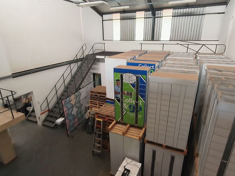 Industrial warehouse space featuring a mezzanine level, metal staircase, and high-pitched roof, currently utilized for storage.