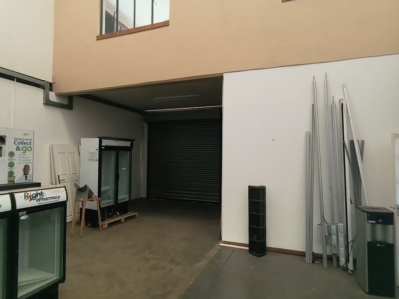 Spacious industrial utility area featuring a high-clearance roller shutter door, mezzanine level access, and concrete flooring, suitable for storage or workshop operations.