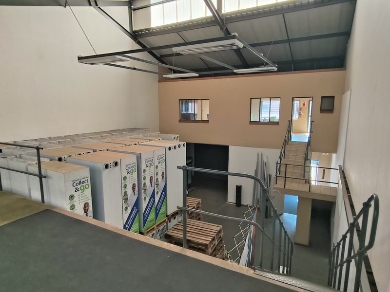 Industrial warehouse space featuring a mezzanine level with metal staircase, steel railings, and high-clearance exposed roof trusses.