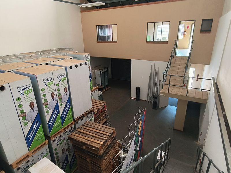 Industrial warehouse space featuring a mezzanine level, metal staircase access, and high-ceiling storage area with roller shutter door access.