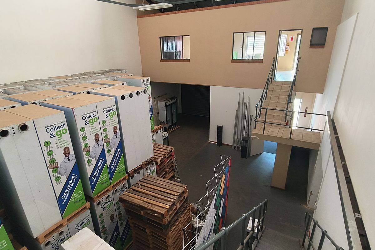 Industrial warehouse space featuring a mezzanine level, metal staircase access, and high-ceiling storage area with roller shutter door access.