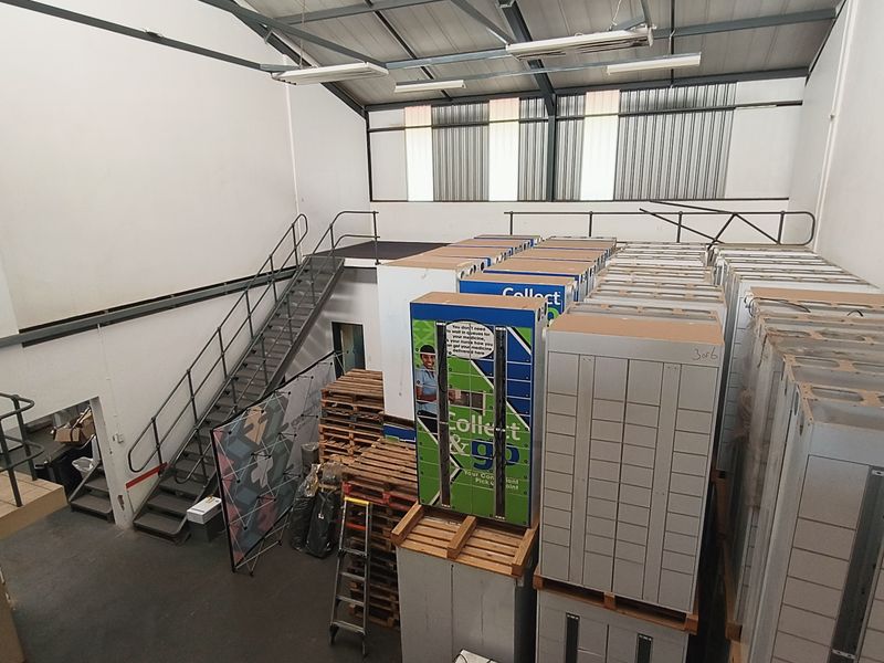 Industrial warehouse space featuring a mezzanine level, metal staircase, and high-clearance steel roof structure, currently utilized for storage.