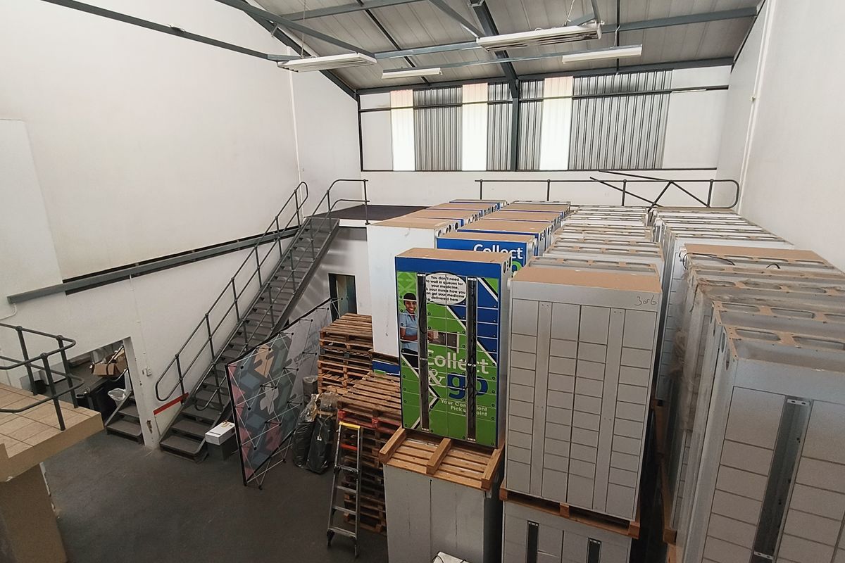 Industrial warehouse space featuring a mezzanine level, metal staircase, and high-clearance steel roof structure, currently utilized for storage.