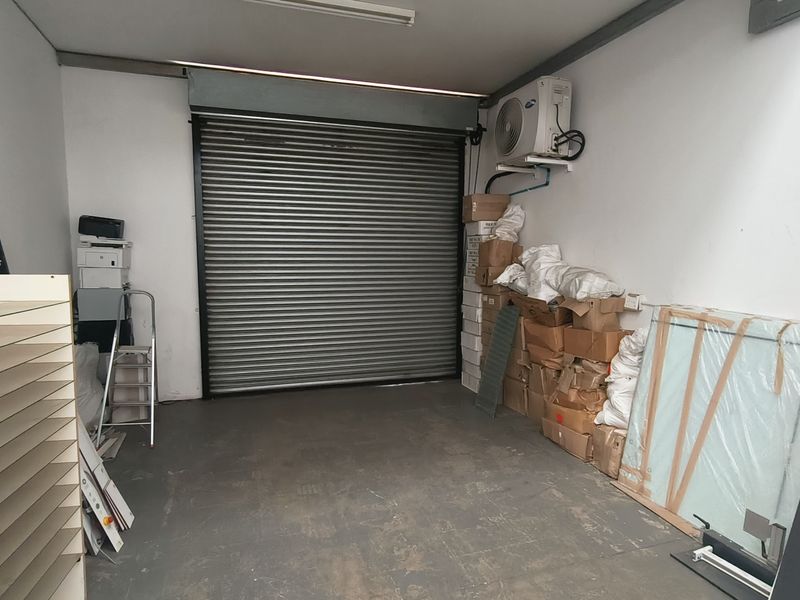 Industrial garage space featuring a secure roller shutter door, concrete flooring, and a wall-mounted air conditioning unit, suitable for storage or workshop use.