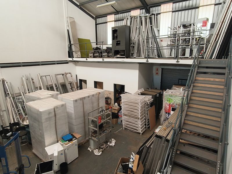 Industrial warehouse space featuring a mezzanine level, steel staircase, and high-clearance ceilings with exposed structural elements.