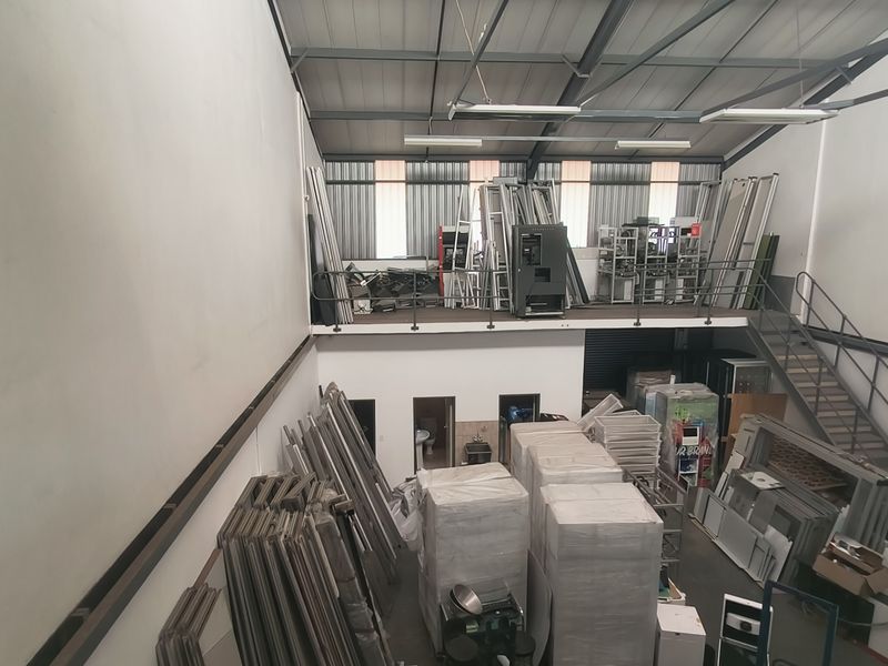 Spacious industrial warehouse featuring a mezzanine level, exposed steel roof structure, metal staircase, and high ceilings suitable for storage or manufacturing operations.