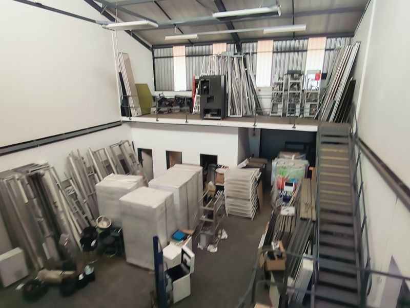 Industrial warehouse space featuring a mezzanine level, metal staircase, and high-clearance ceilings, suitable for storage or manufacturing operations.