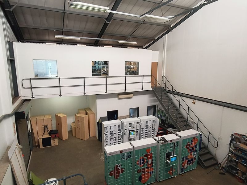 Industrial warehouse space featuring a mezzanine level, metal staircase, and high ceilings with exposed structural elements, suitable for storage or operational use.