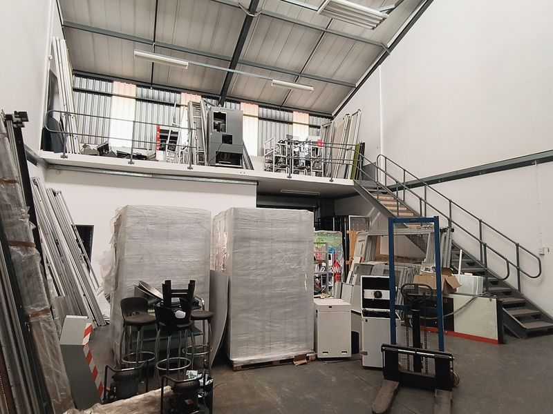 Industrial warehouse space featuring a mezzanine level, metal staircase, high ceilings with exposed steel trusses, and durable concrete flooring.