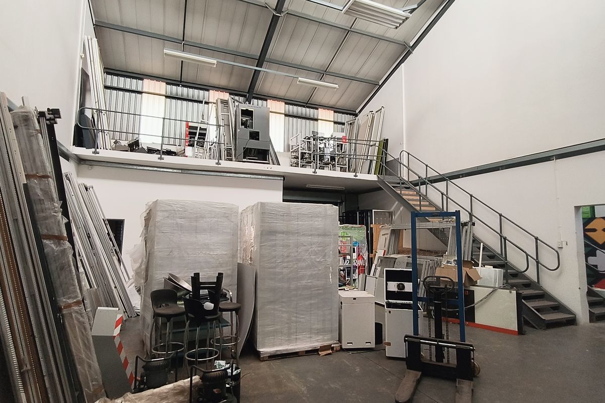 Industrial warehouse space featuring a mezzanine level, metal staircase, high ceilings with exposed steel trusses, and durable concrete flooring.