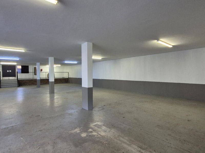 A spacious, open-plan industrial utility area featuring concrete flooring, support columns, and overhead fluorescent lighting, suitable for storage or workshop use.